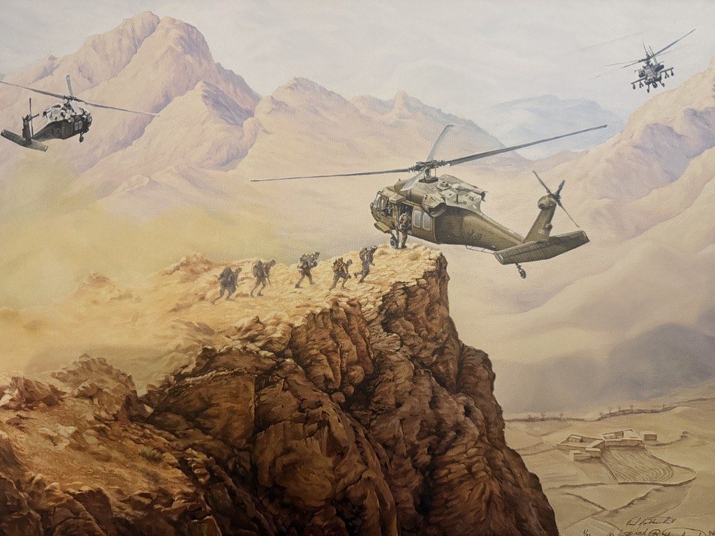 A painting of Black Hawk helicopters flying over rugged desert mountains while soldiers climb a ridge.