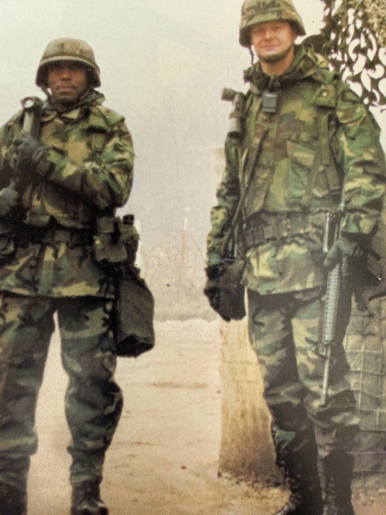 Two soldiers in field uniforms and helmets standing together in Bosnia on Thanksgiving Day guard duty.
