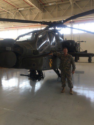 Glenn Wegner standing beside an AH-64 Apache helicopter inside a hangar.